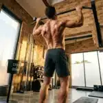 Homme musclé effectuant une traction en salle de sport.