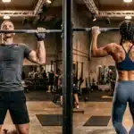 Homme et femme font des tractions à la barre en salle sport.