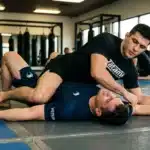 Deux athlètes pratiquent le grappling sur tapis bleu en salle
