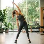 Femme en tenue de sport effectuant un étirement latéral dans un studio fitness moderne